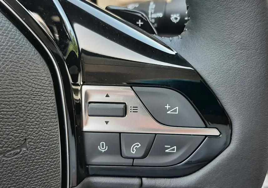 Gros plan sur les commandes multifonctions à gauche du volant en cuir noir du Peugeot 308 gris sélénium.