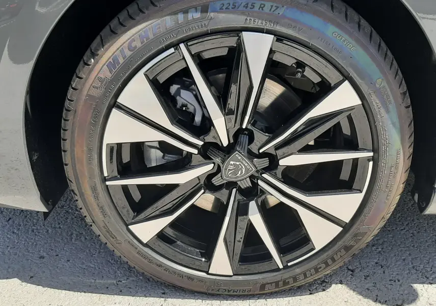 Gros plan sur la jante noire et argentée avec logo Peugeot d'une 308 gris selenium, pneu Michelin visible.
