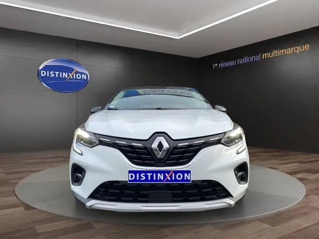 Vue frontale du Renault Captur blanc nacré avec toit noir, calandre noire et phares LED allumés en showroom.