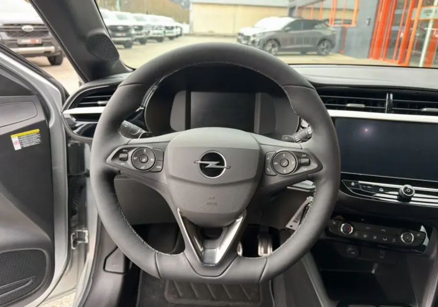Vue intérieure centrée sur le volant cuir multifonctions de l’Opel Corsa Hybrid gris kristall, avec tableau de bord et écran tactile.