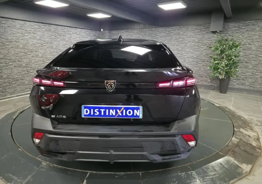 Vue arrière d'une Peugeot 408 électrique noire avec feux LED allumés dans un showroom moderne.