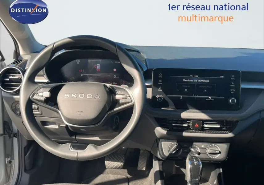 Vue intérieure centrée sur le volant SKODA et le tableau de bord avec écran tactile, ambiance gris noir moderne.