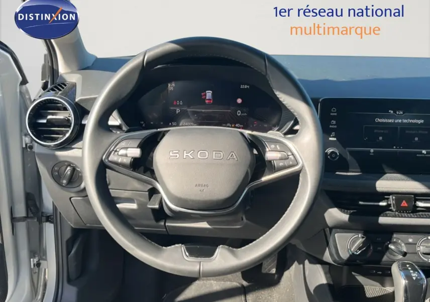 Vue intérieure centrée sur le volant SKODA d'une Fabia 2025, tableau de bord numérique et écran tactile visibles.