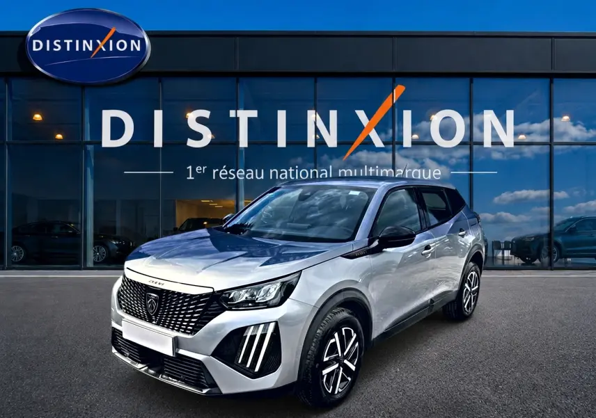 Peugeot 2008 gris en 3/4 avant droit, avec calandre noire et feux LED distinctifs, devant showroom Distinxion.