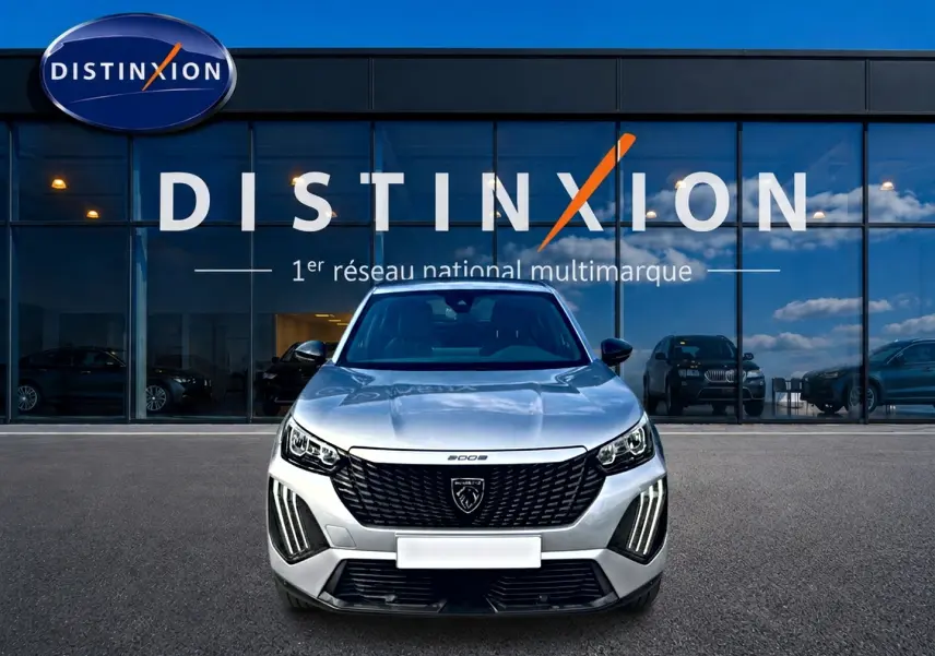 Vue avant d'un Peugeot 2008 gris 2025 avec calandre noire et feux LED verticaux, devant une vitrine Distinxion.
