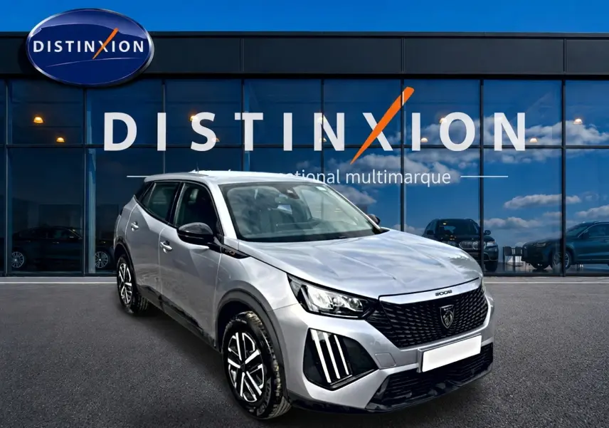 Peugeot 2008 gris en 3/4 avant droit, avec calandre noire et feux LED distinctifs, devant vitrine Distinxion.