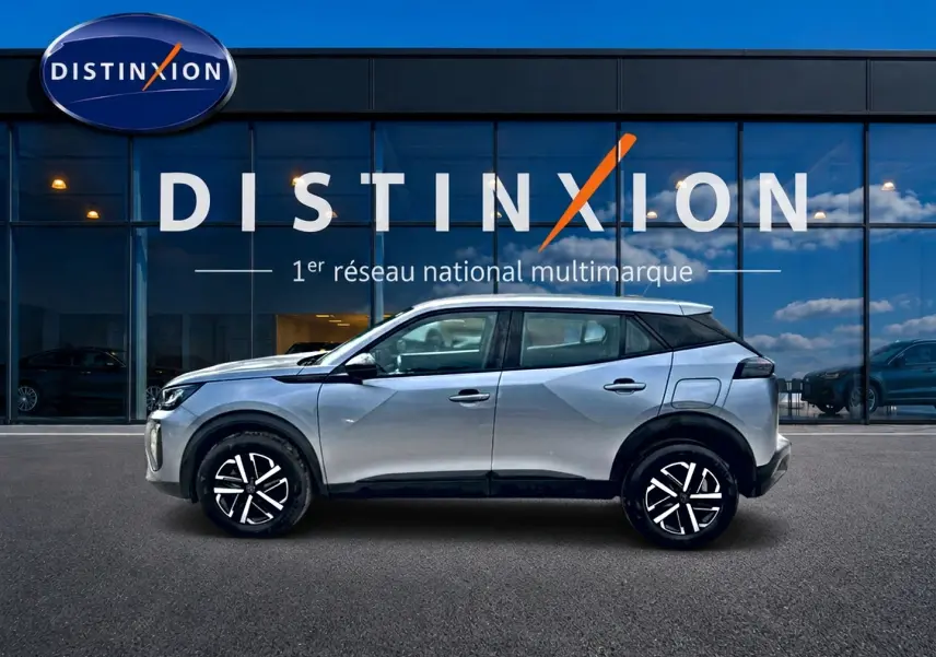 Profil côté gauche d’un Peugeot 2008 gris 2025 avec jantes noires et toit noir devant une vitrine Distinxion.