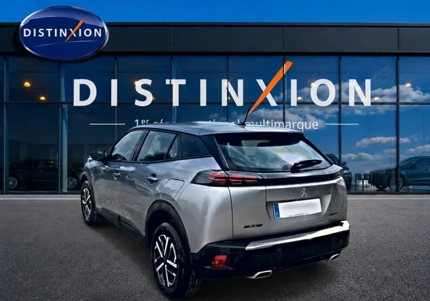 Peugeot 2008 gris en 3/4 arrière droit, avec feux arrière LED et toit noir contrastant, devant un showroom Distinxion.
