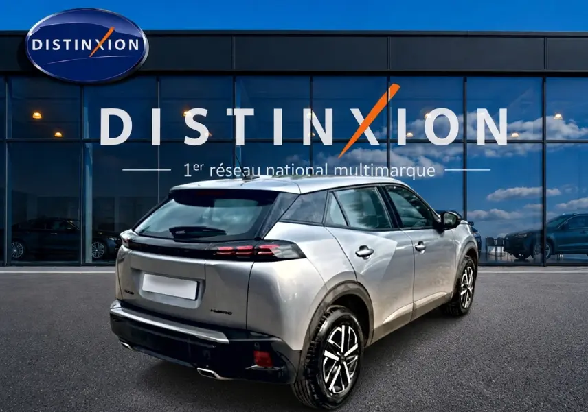 Vue 3/4 arrière droite d'un Peugeot 2008 gris 2025 avec becquet arrière et feux LED, stationné devant une vitrine Distinxion.