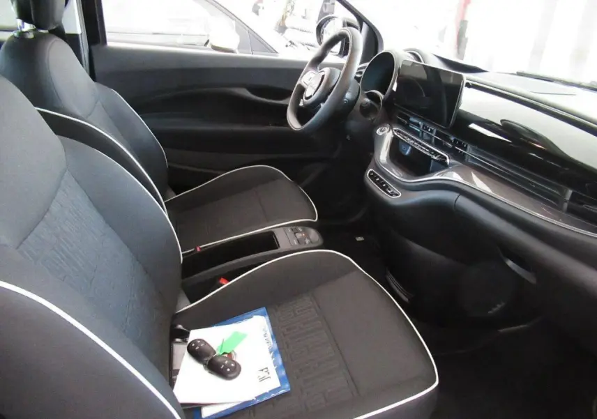 Vue intérieure avant droite de la Fiat 500 Cabriolet électrique 2024, sièges noirs avec surpiqûres blanches et tableau de bord moderne.