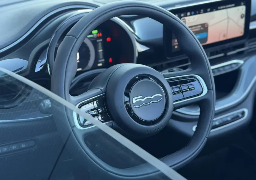 Vue rapprochée du volant noir de la Fiat 500 électrique 2024 avec tableau de bord numérique et écran tactile.