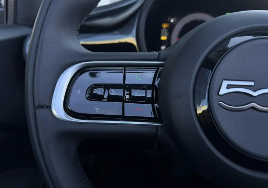 Gros plan sur les commandes gauche du volant noir de la FIAT 500 Cabriolet électrique 2024 avec logo 500 central.