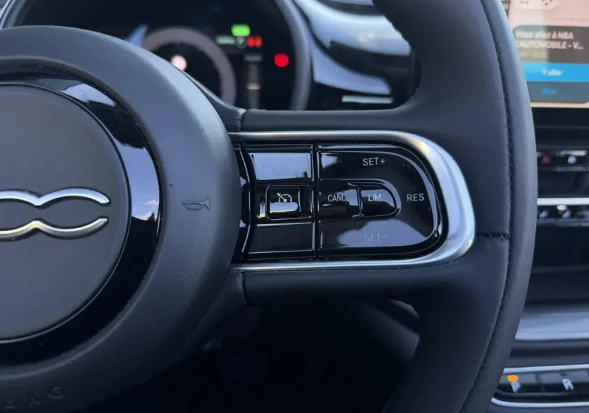 Gros plan sur le volant noir de la Fiat 500 Cabriolet électrique 2024, avec commandes de régulateur de vitesse à droite.