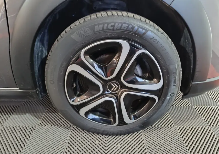 Gros plan sur la roue avant droite d'une Citroën C3 gris foncé, jante noire et argent avec logo Citroën central.