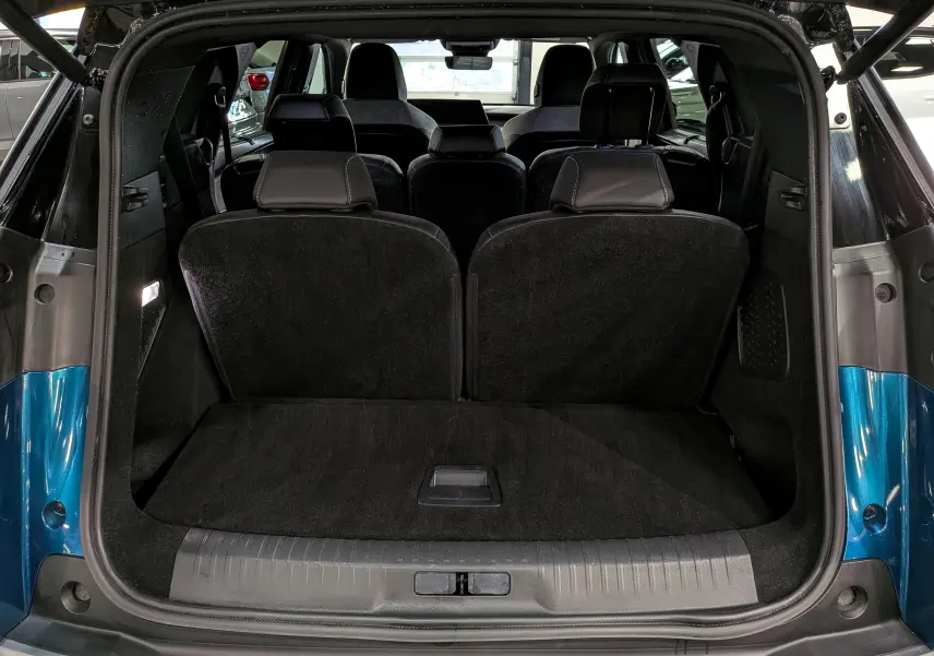 Coffre ouvert vu de l’arrière d’un Peugeot 5008 Hybrid bleu Obsession avec intérieur noir et sièges rabattus partiellement.