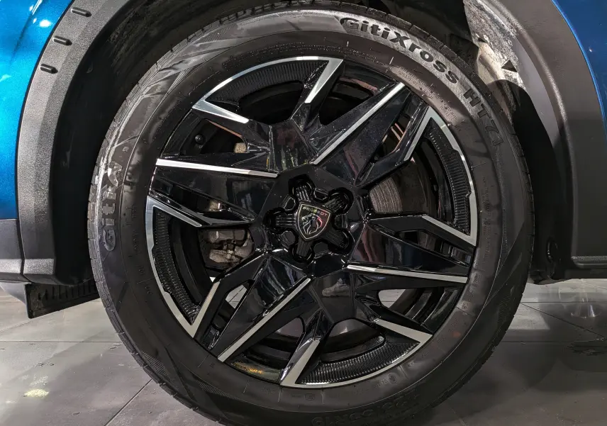 Gros plan sur la roue avant droite du Peugeot 5008 Hybrid 145 GT, jante noire brillante avec détails argentés.