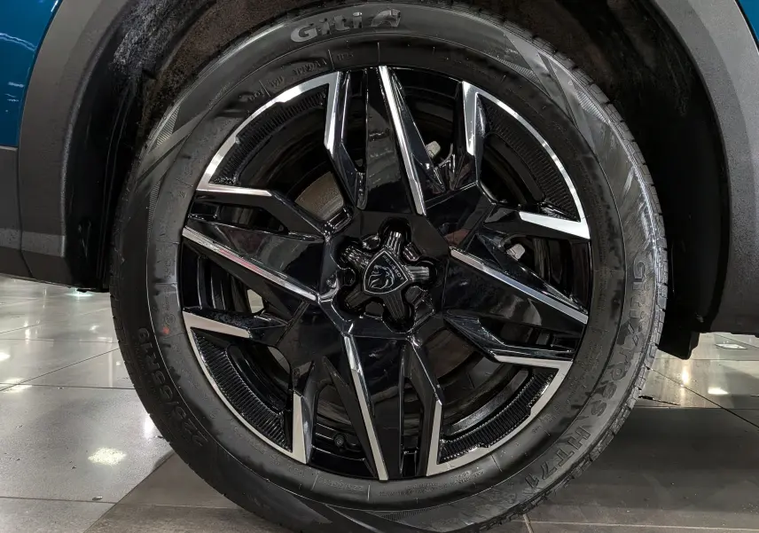 Gros plan sur la roue avant droite du Peugeot 5008 Hybrid 145 GT bleu Obsession avec jante noire et détails chromés.