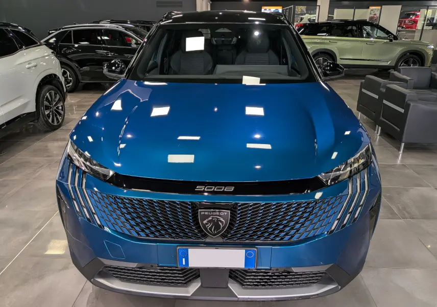 Vue avant frontale du Peugeot 5008 Hybrid 145 CH e-DCS6 GT en Bleu Obsession avec toit noir dans un showroom.