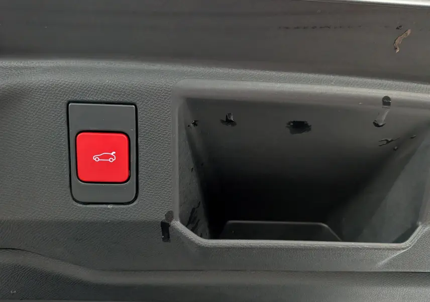 Gros plan sur le bouton rouge d'ouverture électrique du coffre, situé dans le compartiment intérieur noir du Peugeot 5008 Hybrid 2025.