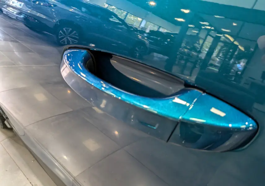 Poignée de porte bleue Obsession en gros plan sur Peugeot 5008 Hybrid 145 CH e-DCS6 GT, reflet du toit noir visible.