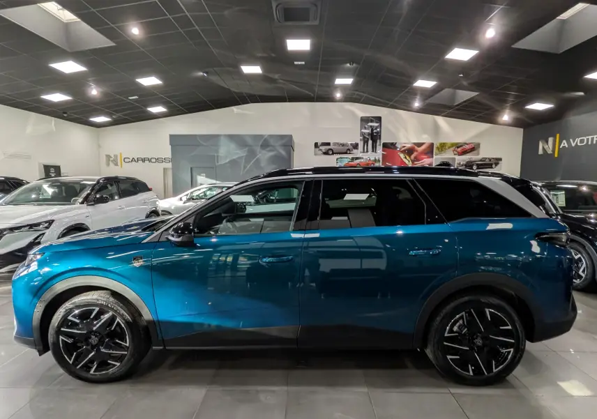 Vue latérale droite d’un Peugeot 5008 Hybrid 145 CH e-DCS6 GT bleu Obsession avec toit noir dans un showroom.