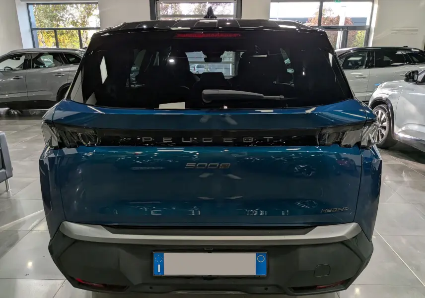 Vue arrière d’un Peugeot 5008 Hybrid bleu Obsession avec toit noir, en intérieur, soulignant son design moderne et épuré.