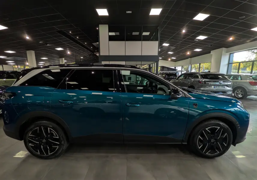 Vue de profil côté gauche d’un Peugeot 5008 Hybrid 145 CH e-DCS6 GT bleu Obsession avec toit noir en showroom.