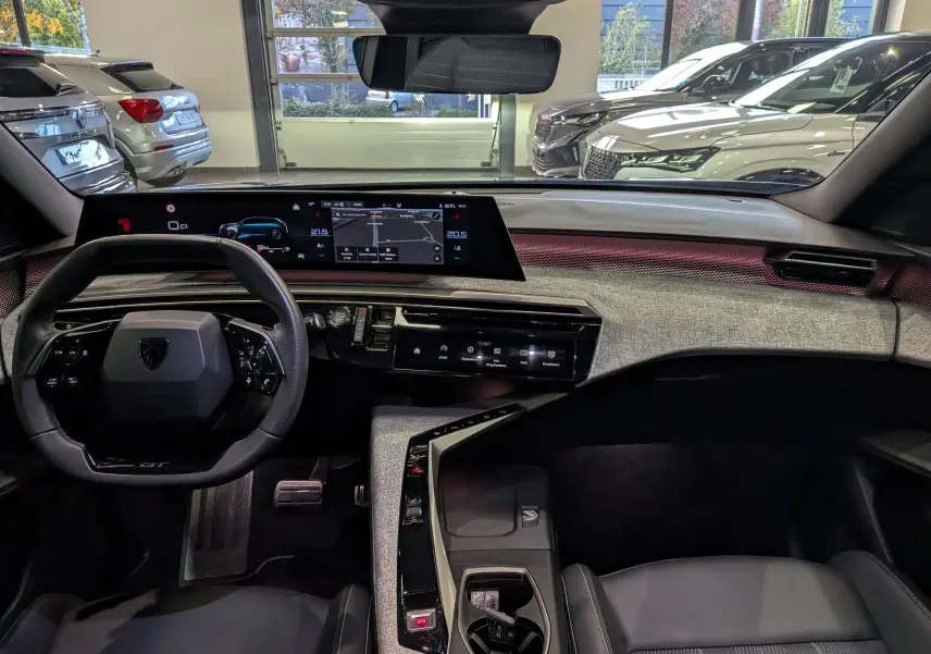 Vue intérieure avant du Peugeot 5008 Hybrid 145 GT 2025, tableau de bord moderne avec écran large et volant compact noir.