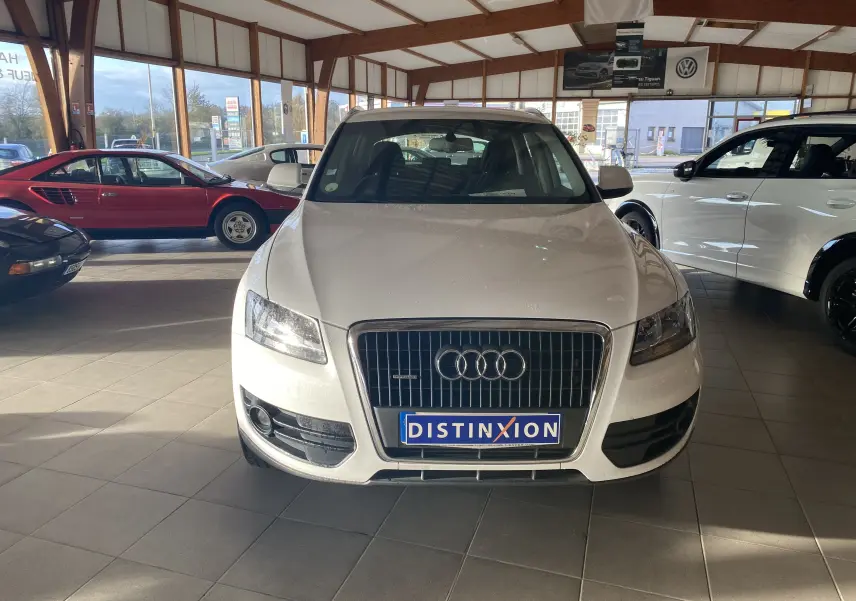 Vue frontale d'un Audi Q5 blanc 2012 en showroom, mettant en valeur la calandre distinctive et les phares allumés.