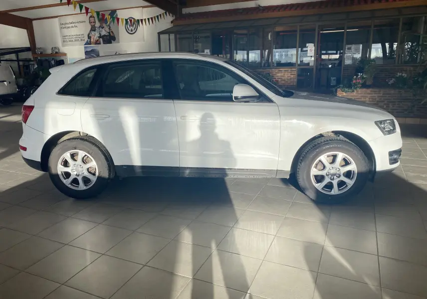 Audi Q5 blanc vue de profil côté gauche, stationné en intérieur avec jantes alliage et pneus visibles.