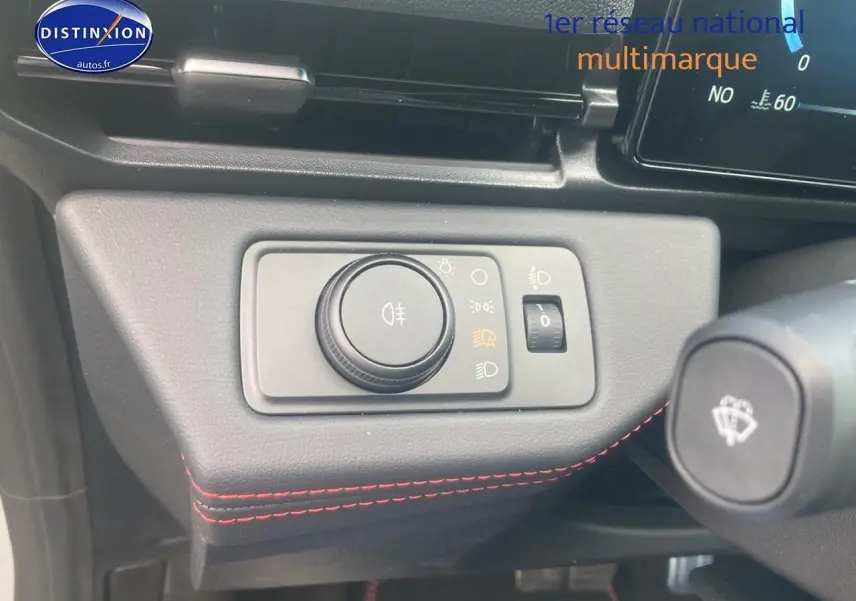 Détail du tableau de bord avec commande des phares et surpiqûres rouges dans une Ford Puma gris cactus 2025.