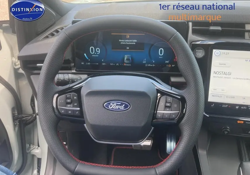 Vue rapprochée du volant perforé avec surpiqûres rouges du Ford Puma gris cactus 2025, tableau de bord numérique visible.