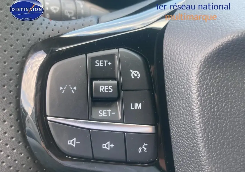 Gros plan sur les commandes du régulateur de vitesse et du volume sur le volant perforé d'un Ford Puma gris cactus.