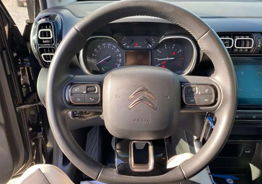 Vue rapprochée du volant en croûte de cuir d'une Citroën C3 Aircross noire, avec tableau de bord et commandes au volant visibles.