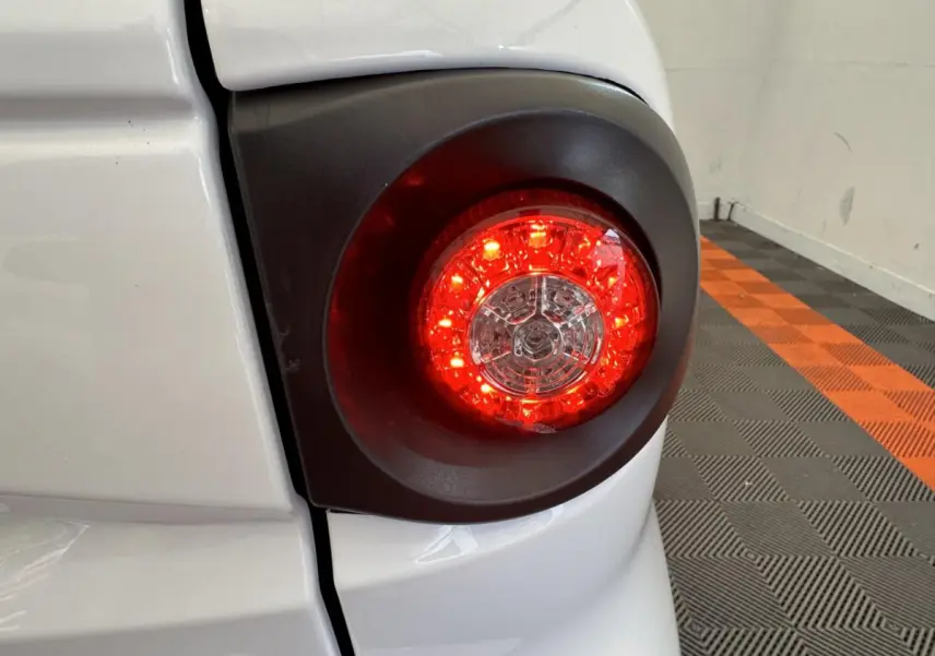 Gros plan sur le feu arrière droit rouge d’une Aixam Minauto E Access blanche, avec carrosserie et sol à damiers orange et gris.