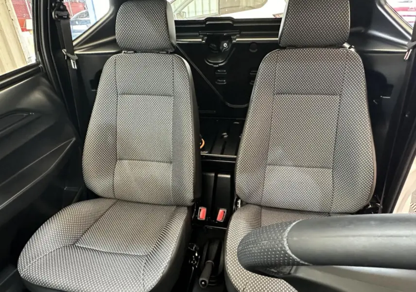 Vue intérieure frontale des sièges avant gris à motifs de l'AIXAM MINAUTO E ACCESS blanc, avec volant partiellement visible côté conducteur.