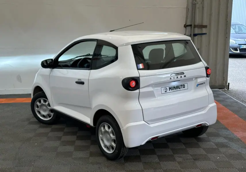 Vue 3/4 arrière droite d'une AIXAM MINAUTO E ACCESS blanche, petite citadine électrique avec feux ronds et caméra côté conducteur.