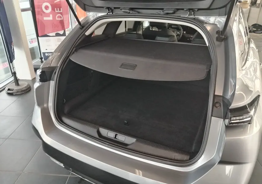 Coffre ouvert vu de l'arrière d'une Peugeot 308 SW Hybrid 145 gris Artense, montrant l'espace de chargement et la tablette cache-bagages.
