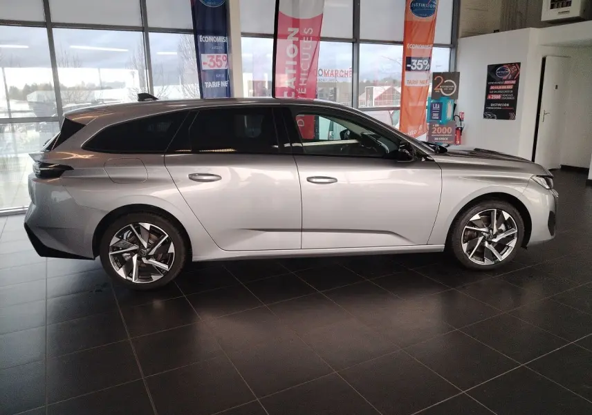 Peugeot 308 SW Hybrid 145 e-DCS6 Allure gris Artense vue de profil côté gauche en intérieur showroom.