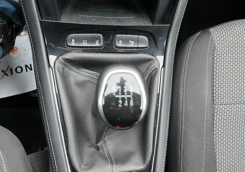 Gros plan sur le levier de vitesses manuel d'un Opel Grandland X gris, avec boutons de commande et siège tissu visible.
