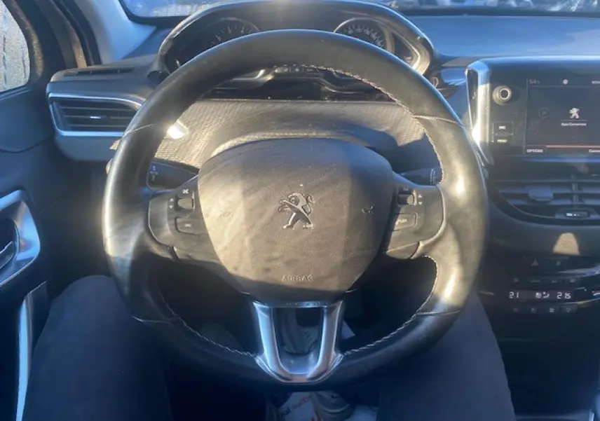 Vue intérieure centrée sur le volant cuir de la Peugeot 2008, avec écran tactile multifonction et tableau de bord visible.