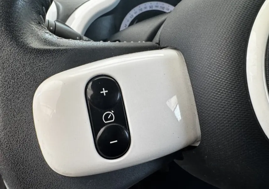 Gros plan sur les commandes blanches du régulateur de vitesse sur le volant cuir noir de la Renault Twingo Intense Energy 2016.