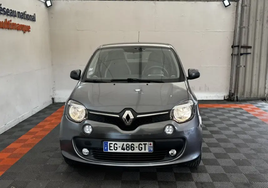 Vue de face d'une Renault Twingo Intense Energy TCe 90 gris foncé avec phares allumés dans un garage.