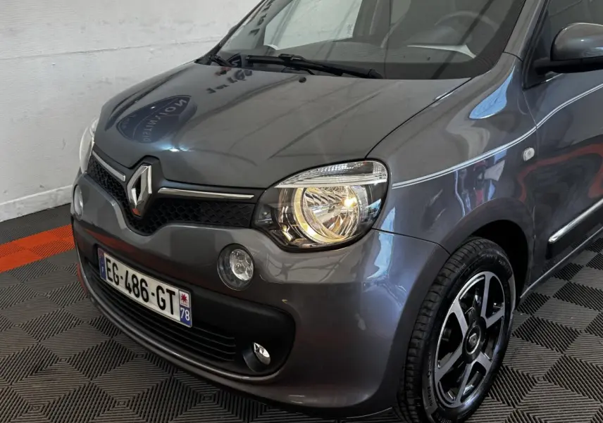 Vue 3/4 avant droit d'une Renault Twingo Intense Energy TCe 90 gris foncé avec phares allumés et jantes noires.