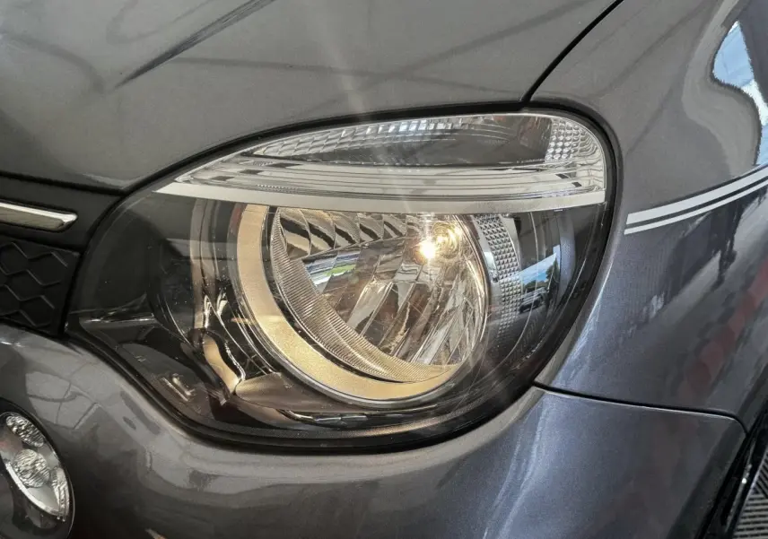 Gros plan sur le phare avant droit d'une Renault Twingo Intense Energy TCe 90 gris foncé avec bande décorative blanche.