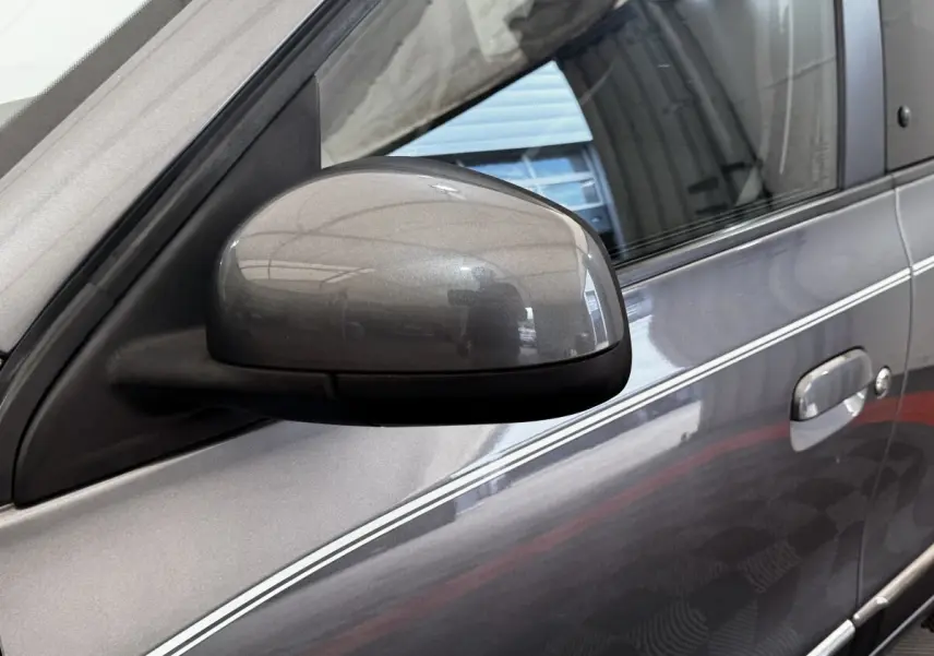 Gros plan sur le rétroviseur côté conducteur d'une Renault Twingo gris foncé avec bande blanche décorative sur la porte.