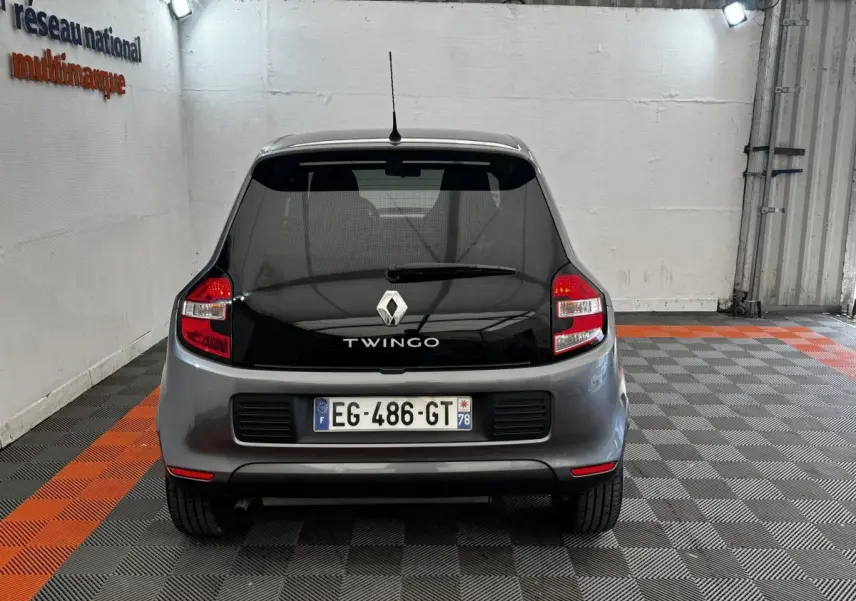 Vue arrière d'une Renault Twingo gris foncé avec vitre arrière noire et feux arrière rouges dans un garage.
