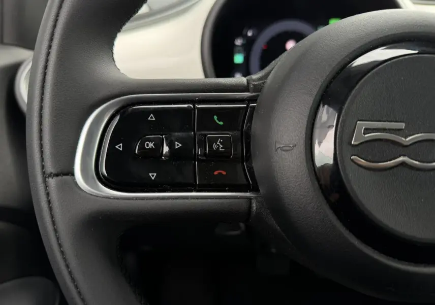 Gros plan sur le volant noir du Fiat 500 électrique 2024, avec commandes intégrées et logo 500 au centre.