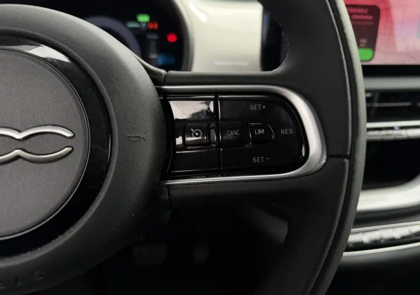 Gros plan sur le volant noir Soft-Touch de la Fiat 500 électrique, avec commandes de régulateur de vitesse visibles.