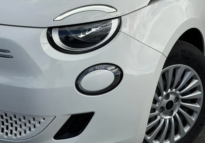Gros plan sur l'avant droit blanc Artic du FIAT 500 électrique, mettant en valeur le phare rond et la jante alliage.